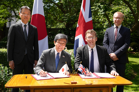Four men, two sitting and two standing, around a table signing a document