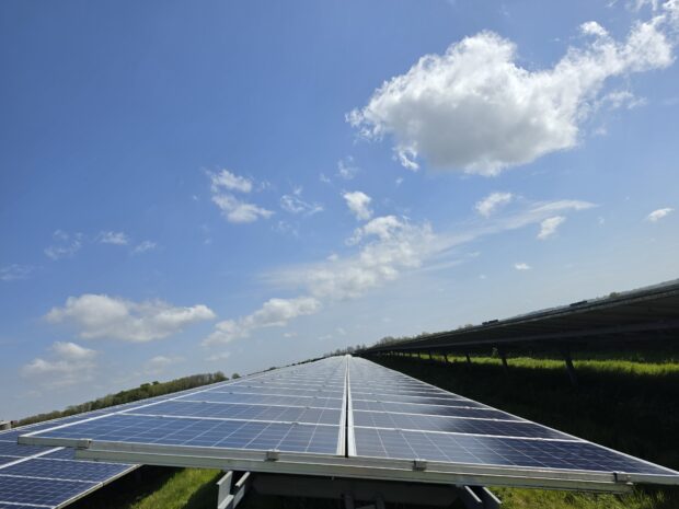 Large solar panels in a green field, under a blue sunny sky with a few clouds.