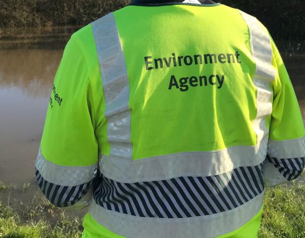 Back of man in Environment Agency high visibility jacket looking across river