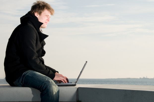 Man wears coat and wortks with laptop at the sea
