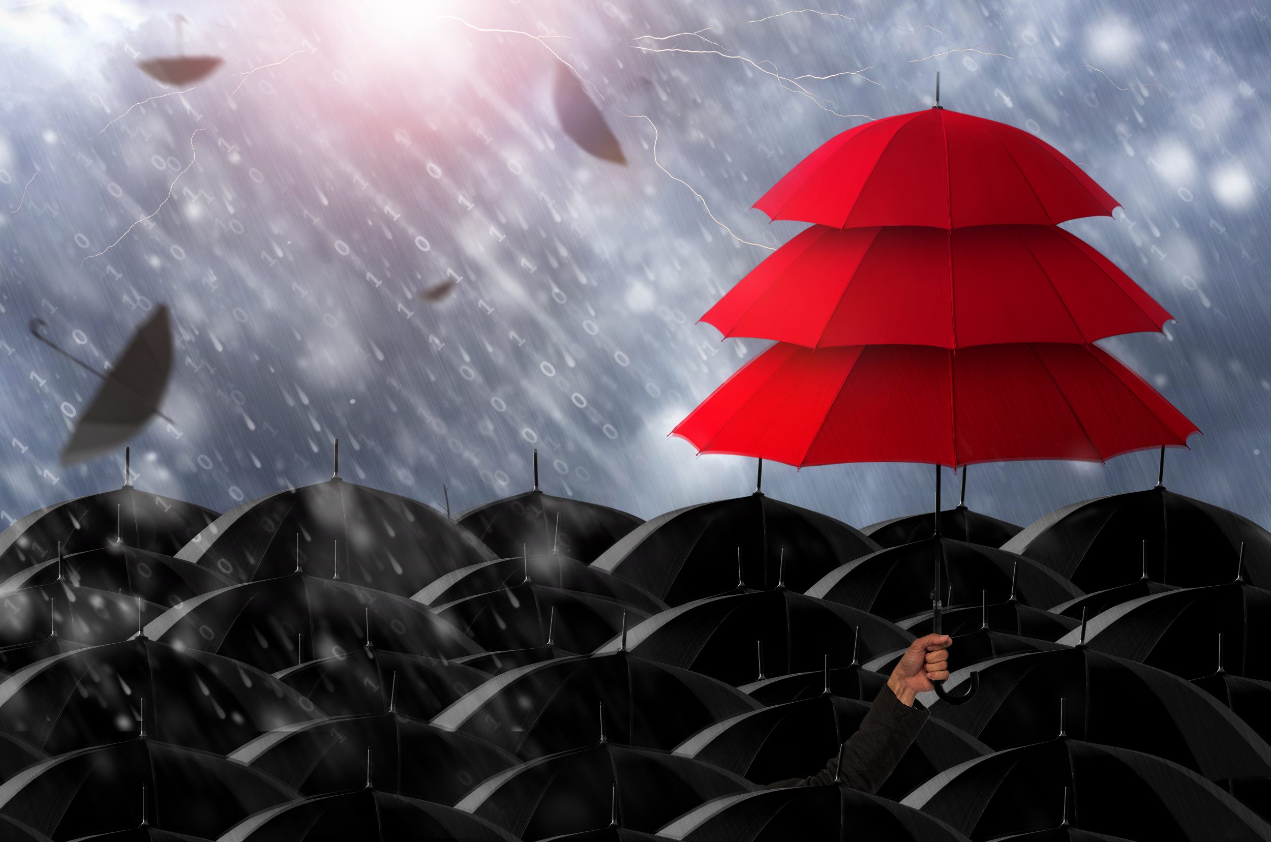 Stack of 3 red umbrellas above loads of black umbrellas in the rain.