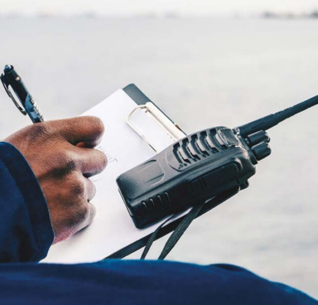 An engineer stands with a notepad and walkie talkie.