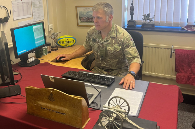 Charles sits at a desk on a computer, this time wearing uniform.