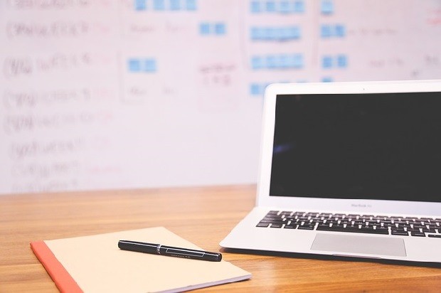 Blank notepad and pen on a desk, beside a laoptop displaying a blank screen