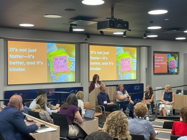 A panel discussion at the first Test, Learn and Grow event. Behind the panel is a screen with a slide that says 'It's not just faster - it's better and it's kinder'.