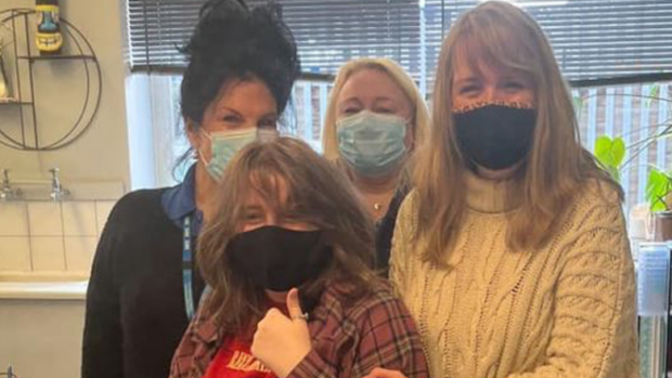 An image of four women at a vaccination centre. Three women stand around Harry's sister who is seated on a chair. All four women are wearing masks. Harry's sister Lily sat giving a thumbs-up to the camera.