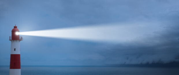Lighthouse shining a beam of light across a dark sea.