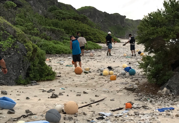 This image shows the terrible damage that global marine pollution is having on a UK Overseas Territory. Image of five individuals amongst litter on a beach