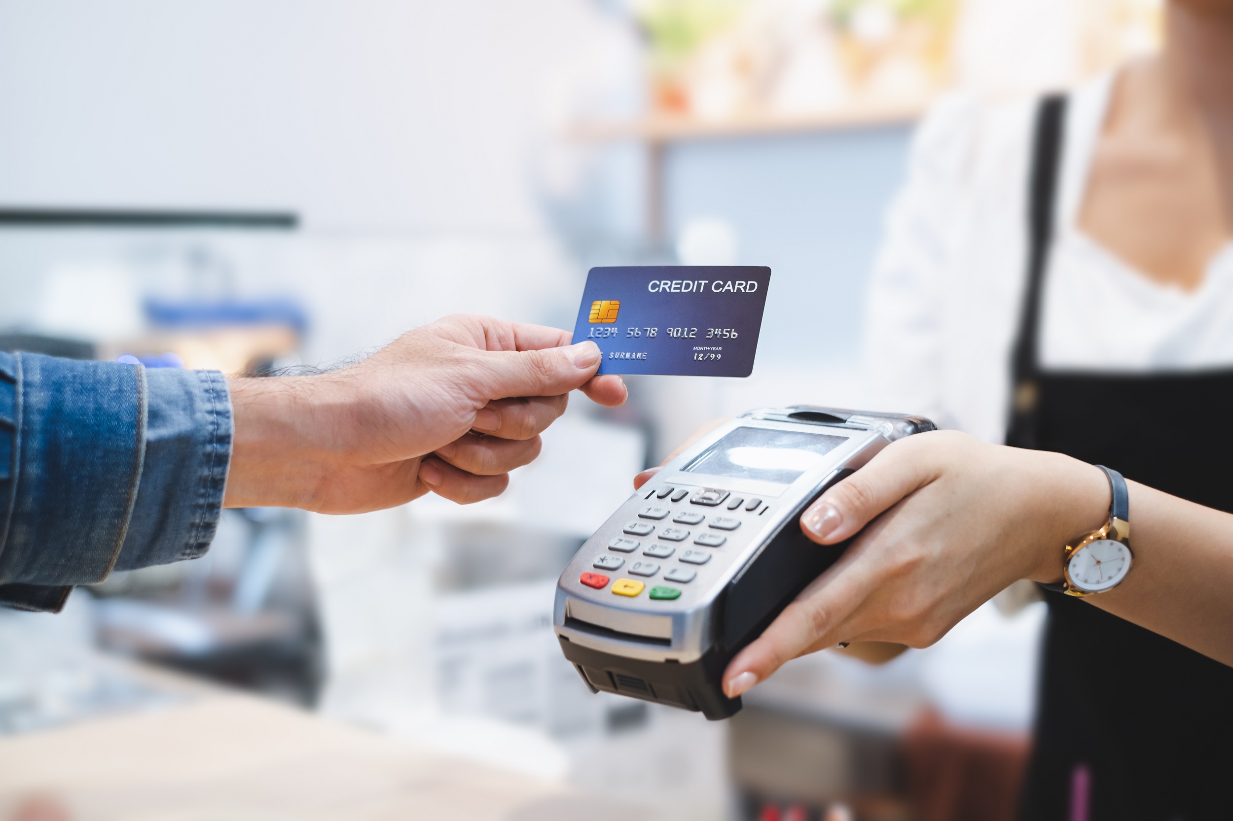 Close up of man's hand as he holds a credit card towarsds a card reader which is being held by a woman who is blurred out