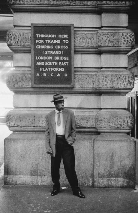 A man standing in front of a sign that says 'Through here for trains to Charing Cross London Bridge and South East Platforms