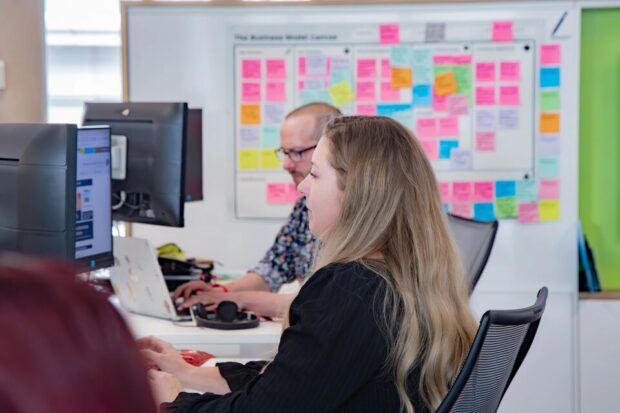 Office employee using a computer at her desk with a colleague in the background