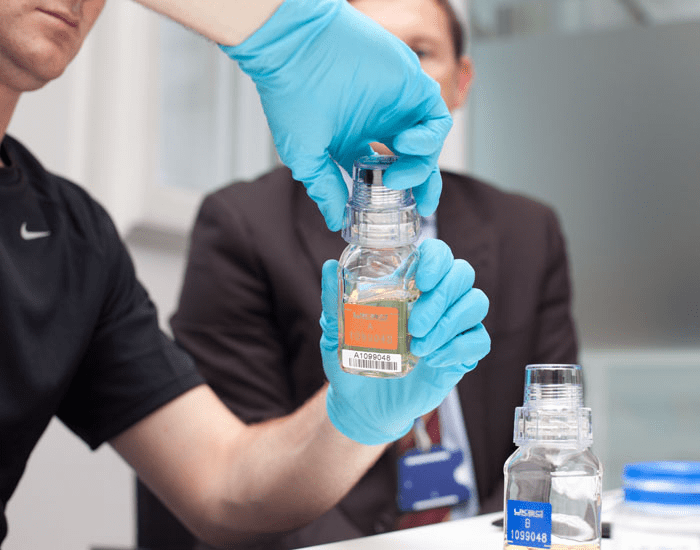 A urine sample collection pot being sealed by a member of Doping Control Personnel wearing gloves