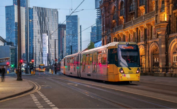 A tram in Manchester surrounded by a mixture of Victorian and modern architecture.