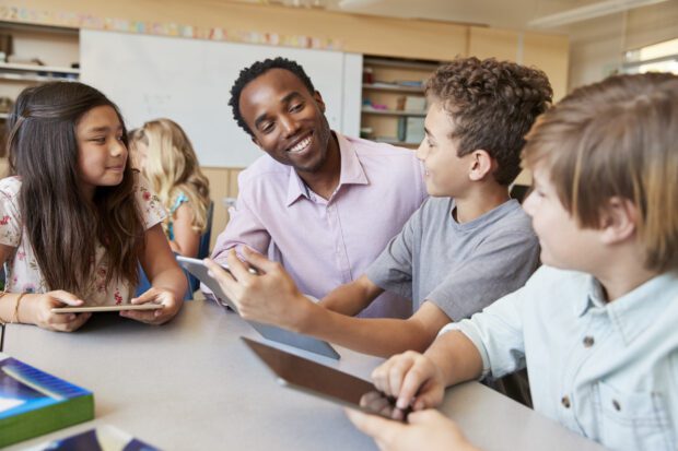 Teacher talking to primary school pupils, who are holding tablets.