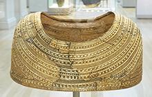 A gold cape to be placed through head and sit on shoulders. 
