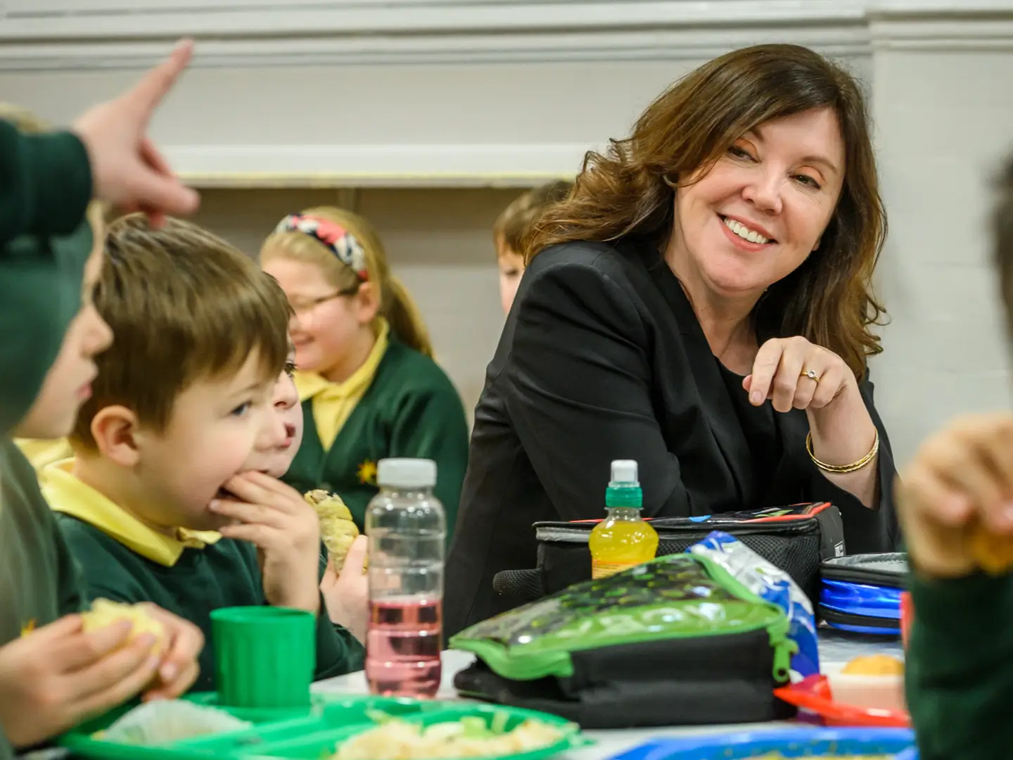 Dame Rachel de Souza sitting at a school lunch table with children