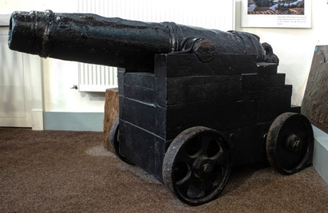 Modern digital colour photograph of a black cannon displayed indoors on a black wheeled gun carriage
