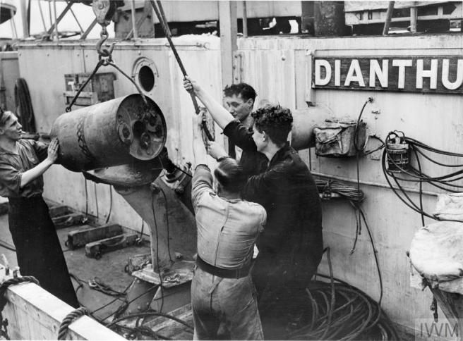 Historic black & white photograph of four young men hoisting a depth charge onto a depth charger.