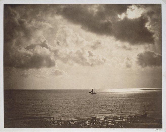 Victorian sepia photograph of ship seen from afar all alone on a calm sea, sunlight striking the sea to the right of the ship from among the clouds.,