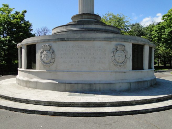 Modern colour photo of circular base of memorial, the text flanked on either side by the badge of the Royal Naval Patrol Service, an anchor in a shield encircled by laurel and oak leaves