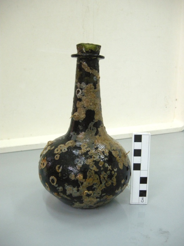 An archaeological record view of a rounded glass bottle with a scale rule adjacent.