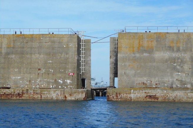 Modern colour photograph of the ends of two concrete Mulberry Harbour structures at sea, exposing their respective staircases, with a ship visible in the gap between them.
