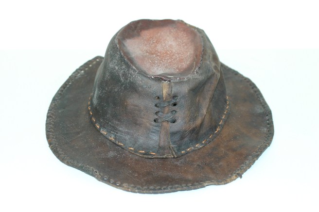 View of brown leather hat against a white background, showing that the crown of the hat is laced together with a decorative thong.