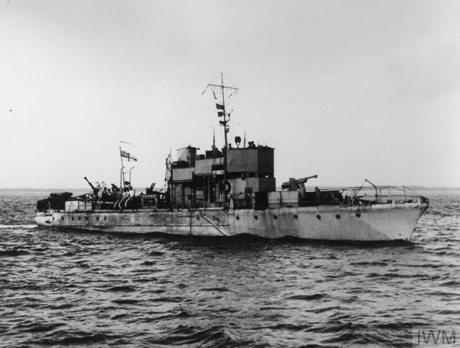 Historic B&W photograph of ship seen in starboard profile view at sea, her guns visible fore and aft, and appearing rather battered.