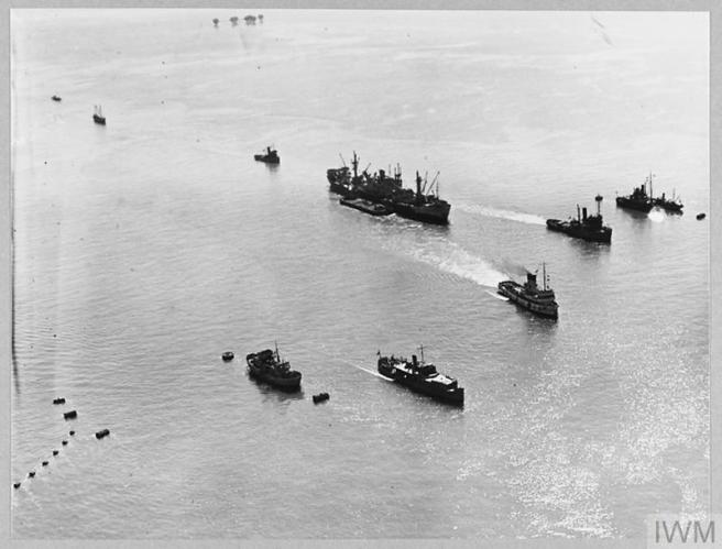 Historic black & white aerial photograph of large ship at centre towed by three smaller vessels to the right