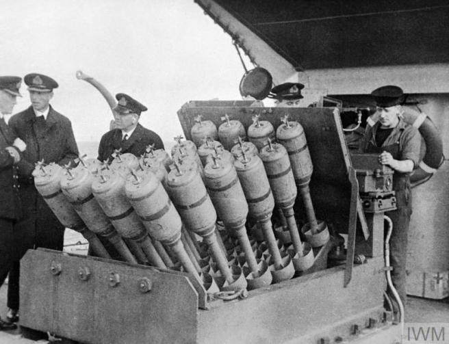 Historic black & white photograph of men operating the mortar with officers looking on to the left.