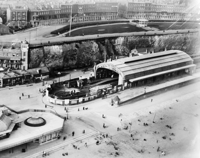 Historic B&W aerial photograph of Ramsgate Harbour Station, showing people walking straight from the station onto the beach; a park and genteel terraces in the town are shown in the upper register of the image