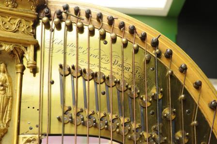 Detail view of top of harp, showing strings and pegs with engraved lettering on a metal plate underneath.