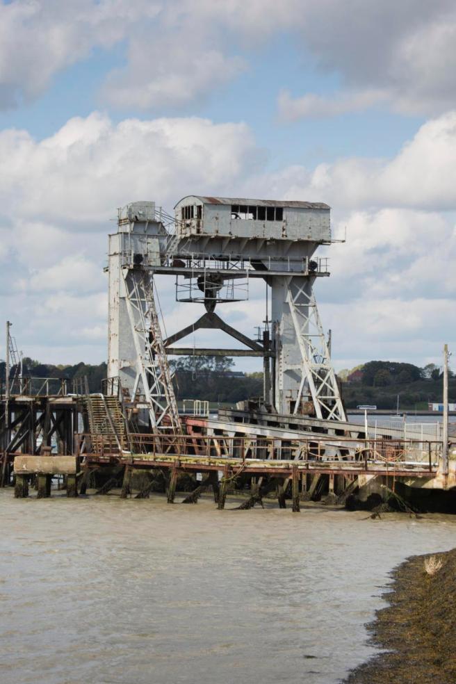 Modern colour photograph of the 1923 gantry, painted in grey, and rusty dock infrastructure, under a cloudy sky.