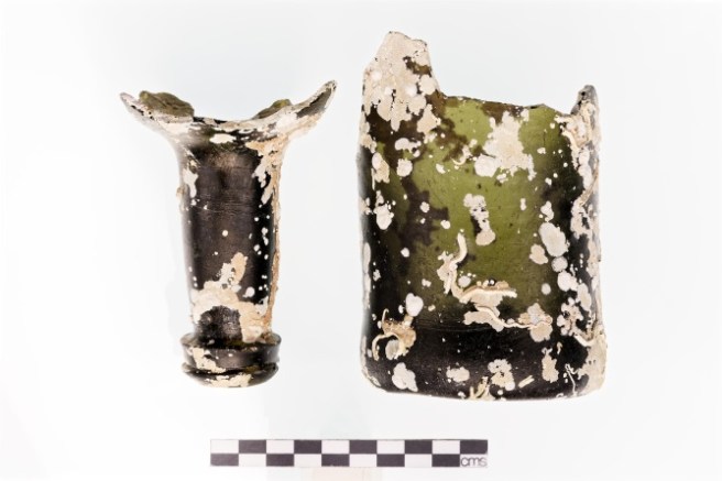 Fragments of green glass bottle with white concretions, scale rule below.