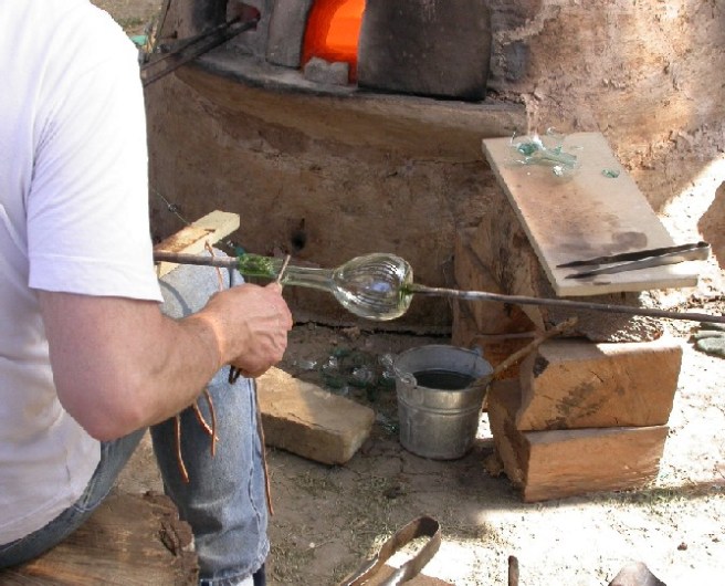 Man working glass in a workshop, with the furnace in the background