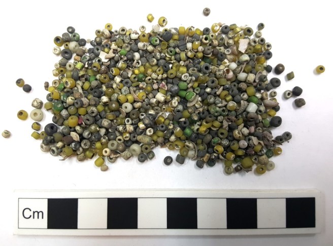 Beads in various shades of green with a scale rule underneath.