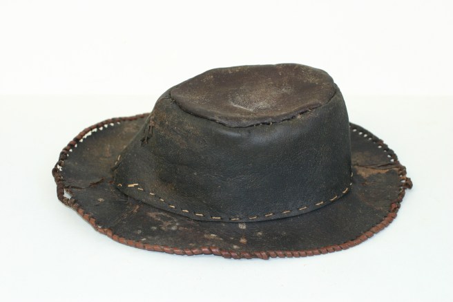 Side view of crown and brim of brown leather hat, against a wide background.