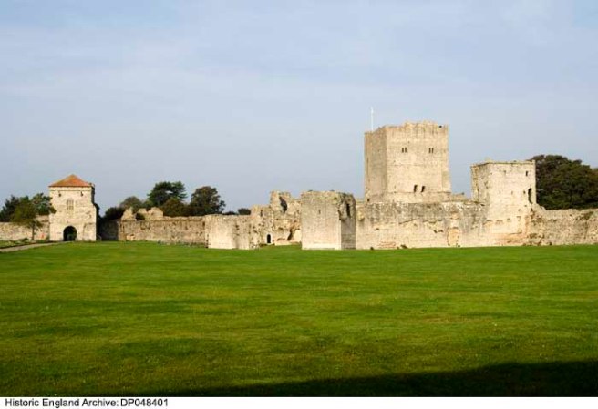 Ruins of castle set against a blue sky, green lawn in foreground.