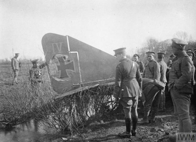 Men in military uniform examining the damaged tail of a downed aircraft, with IV and an Iron Cross legible on the side.