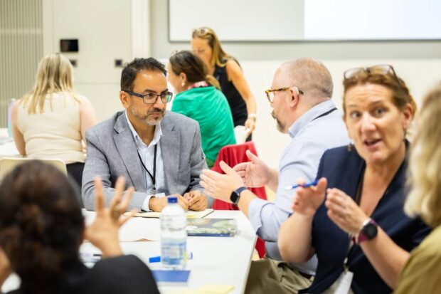 Several people sitting at a table at a workshop. Everyone is in active conversation in pairs.