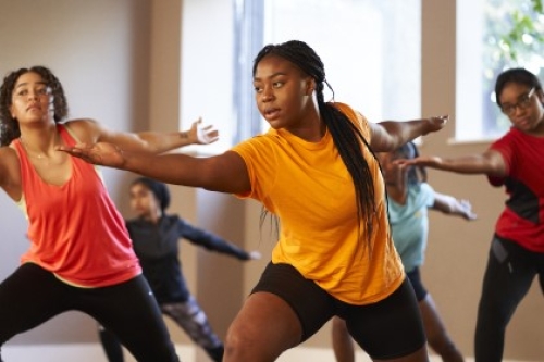 A group of women perform the warrior pose during a yoga class in a studio.