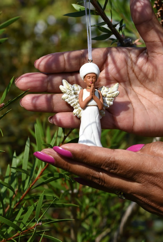 A March Muses angel figurine with darker skin tone, hanging on a tree.