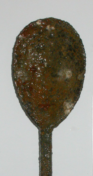 Bowl of a spoon, darkened with age and contact with water, against a plain grey background.