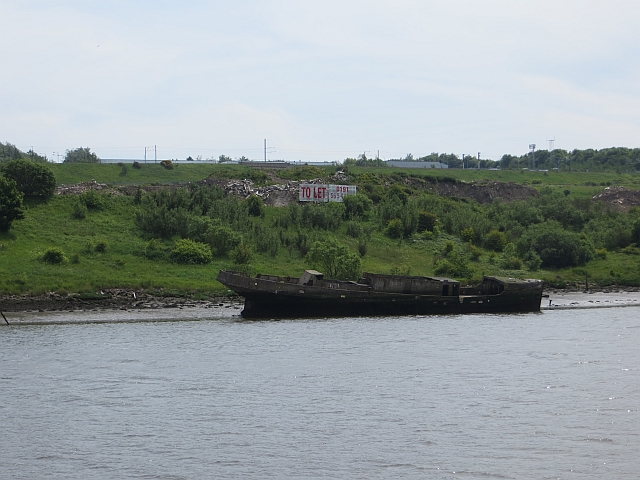 Modern colour photograph of the River Wear in the foreground, with the dark shape of a concrete wreck against the backdrop of the green riverbank on the far side.