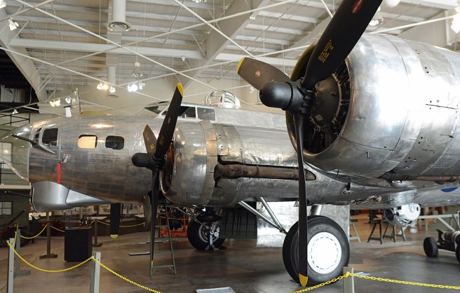Nose and two engines of silver aircraft inside a hangar with white roof.