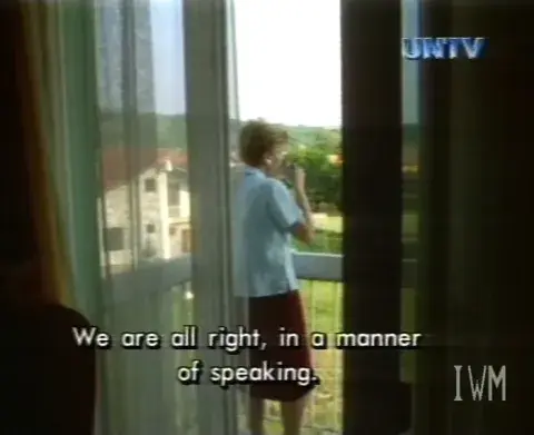 Screenshot of a video letter. A refugee looks out over her balcony. The subtitle reads 'We are alright, in a matter of speaking'.