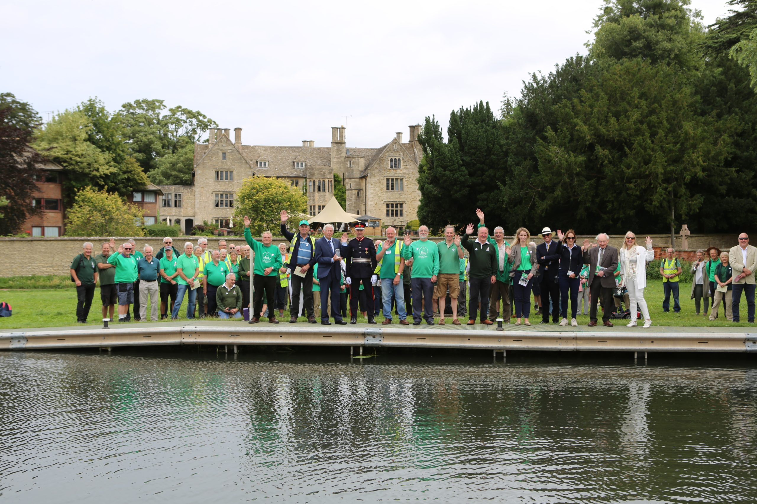 Group of people standing on the opposite side of a canal smiling and waving at the camera.