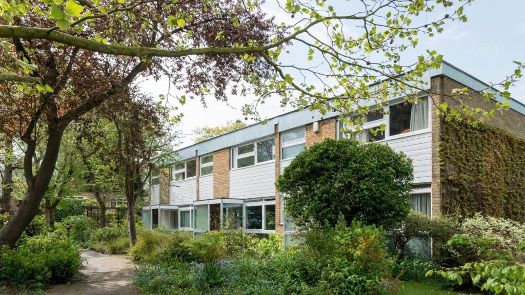 Colour photo showing a view along a 2-storey residential building with planted flowerbeds and overhanging trees in the foreground.