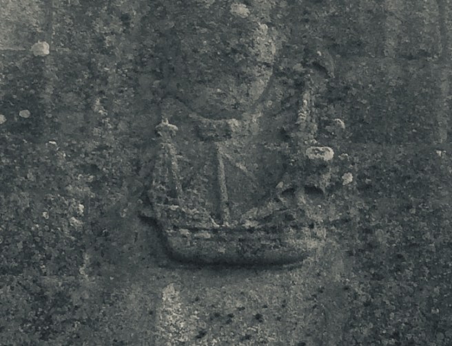 Modern black & white photo of a stone ledge on a wall with a carved relief of a sailing ship.