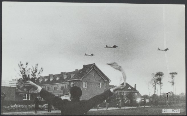 Black & white photo of Dutch citizen waving at three aircraft flying low over a town.